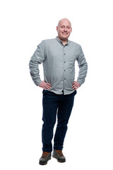 Smiling bald man. A guy in a gray shirt and blue trousers stands with his hands on his belt. Positive and optimistic. Full height. Isolated on a white background. Vertical.