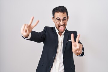 Handsome business hispanic man standing over white background smiling with tongue out showing fingers of both hands doing victory sign. number two.