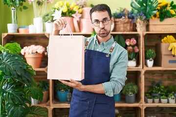 Handsome hispanic man working at florist shop puffing cheeks with funny face. mouth inflated with...
