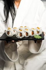 A young woman in a white robe holds rolls in her hands.Hands hold sushi.Japanese cuisine concept