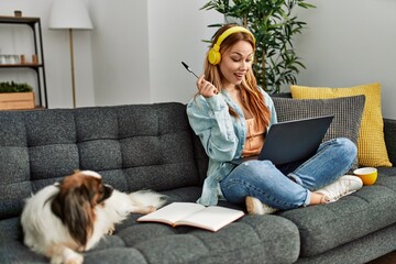 Young caucasian woman sitting on sofa with dog studying at home