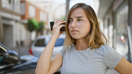 Urban loneliness, beautiful, young caucasian woman, attractively casual yet worried, standing outside on a city street, absorbing a serious voice message on her phone