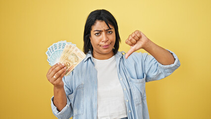 Middle-aged woman showing displeasure with brazilian currency against yellow background.