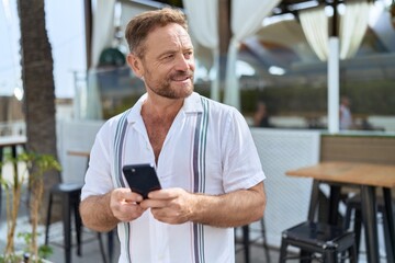 Middle age man smiling confident using smartphone at coffee shop terrace