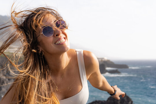 woman smiling looking at camera, with hair blown by the wind, in beach