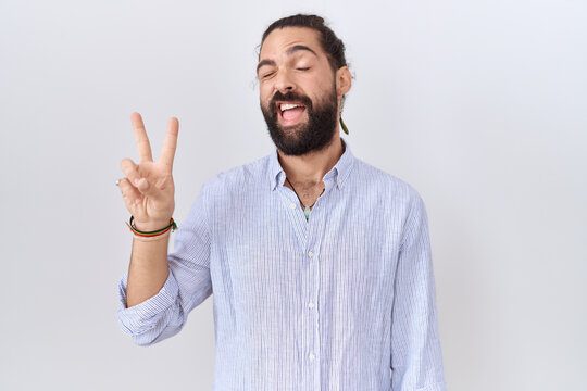 Hispanic man with beard wearing casual shirt smiling with happy face winking at the camera doing victory sign with fingers. number two.