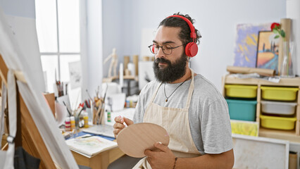 Fototapeta na wymiar Handsome bearded hispanic man with headphones painting in a bright art studio