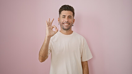 Cheerful young hispanic man confidently flashes an ok gesture, standing isolated over a suave pink...