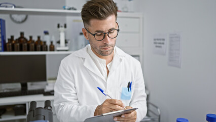 Handsome young hispanic man, charismatic scientist engrossed working, writing a research report in...