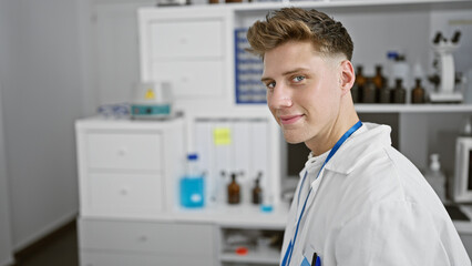 Smiling confident caucasian young man, a handsome scientist, sitting in his lab enjoying the research work. indoors, surrounded by test tubes, a microscope - totally in his element!