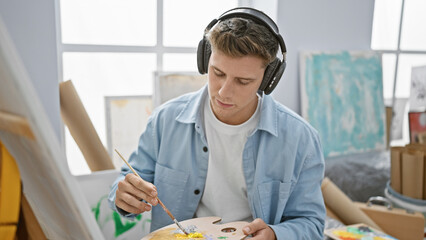 Young caucasian man artist drawing focused listening to music at art studio