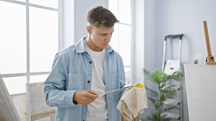 Handsome young caucasian man, a concentrated artist, meticulously cleaning paintbrushes at the...