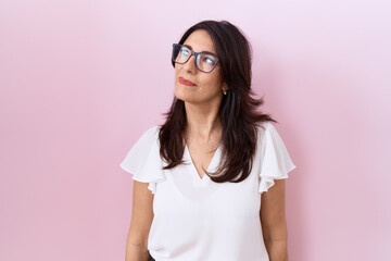 Middle age hispanic woman wearing casual white t shirt and glasses smiling looking to the side and...