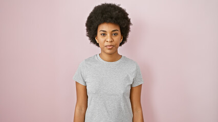 Portrait of a confident adult black woman with curly hair against a pink background in casual...