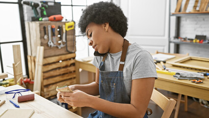 African woman counts money while talking on phone in a carpentry workshop