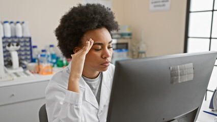 A tired african american woman in a lab feeling stressed while working on a computer