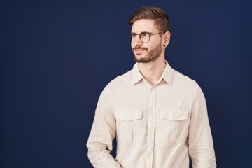 Hispanic man with beard standing over blue background smiling looking to the side and staring away thinking.