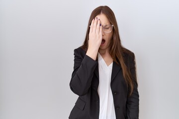 Beautiful brunette woman wearing business jacket and glasses yawning tired covering half face, eye...