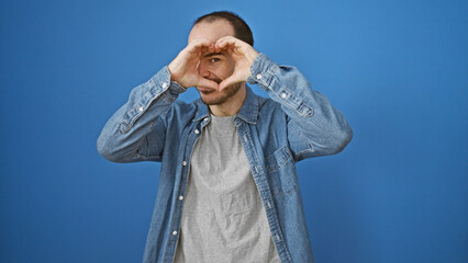 Hispanic bald man with beard making heart shape with hands against blue background