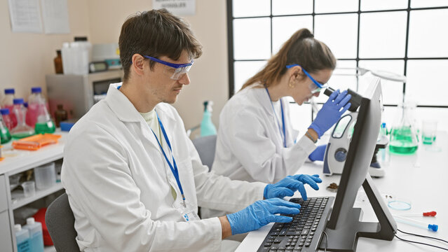 A woman and man in a laboratory working on research with a microscope and computer, depicting teamwork in science.