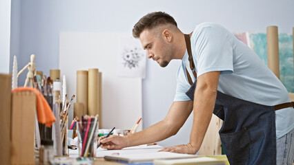 A focused young man with a beard sketches in a bright art studio, embodying creativity and...