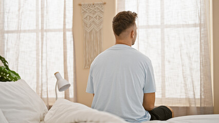 A young hispanic man sits thoughtfully in a tranquil bedroom, exuding casual comfort and...