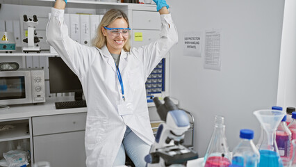 A joyful young woman scientist celebrates in a laboratory setting, surrounded by equipment and...