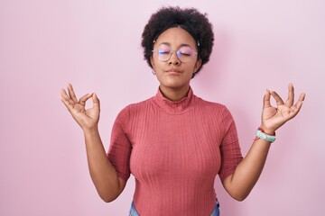 Beautiful african woman with curly hair standing over pink background relaxed and smiling with eyes closed doing meditation gesture with fingers. yoga concept.