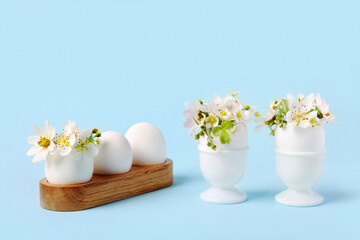 White eggs in wooden and white stands with spring pear and strawberry flowers on a blue background. Happy Easter