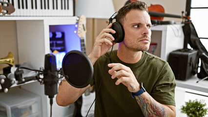 Focused man with headphones in music studio adjusting microphone for recording session