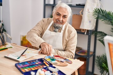 Middle age grey-haired man artist smiling confident mixing color on palette at art studio