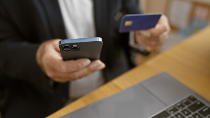 Senior executive man's hands engaged in online shopping with credit card on smartphone at office desk