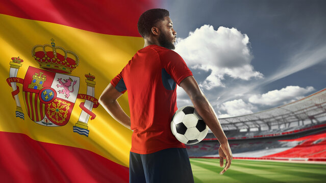 Young African man, soccer payer in red uniform standing on filed with ball, representing team of Spain. 3D arena. Concept of live sport event, championship, match and tournament