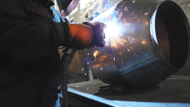 Welder doing joint between two steel details. Man welding parts of the metal detail together. Worker in protective mask welding metal construction at metalworking factory. Slow motion Close up