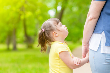 Little girl with syndrome down holds mother's hand at sunny summer park