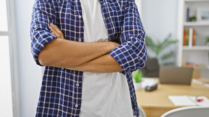 Confident young arab man asserts his success in business world, standing with crossed arms in office, exuding professionalism