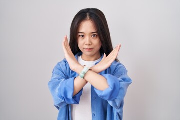 Young chinese woman standing over white background rejection expression crossing arms doing...