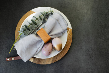 Happy Easter holiday concept. Flat lay photo of marble plate, easter eggs, cutlery and branches of eucalyptus on dark background table. - 739903962
