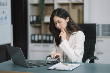 business woman sitting at her desk, reading stats and graphs on paperwork at the office.