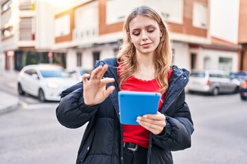 Young blonde woman smiling confident using touchpad at street