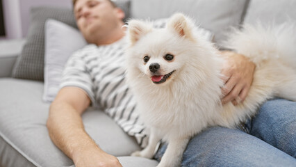 Young caucasian man with dog lying on sofa sleeping at home
