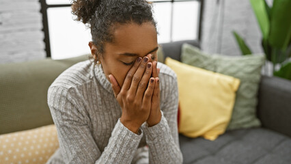 Worried young woman sitting with hands on face in a cozy living room interior.
