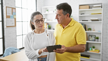 Relaxed hispanic man and serious woman working together in office, concentrated business workers using touchpad for online success