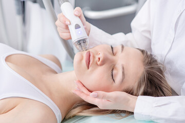 Obraz na płótnie Canvas Pretty young woman client lying with closed eyes and getting stimulating beauty facial treatment during rf-lifting and vacuum massage procedure at clinic. Radiofrequency face lifting