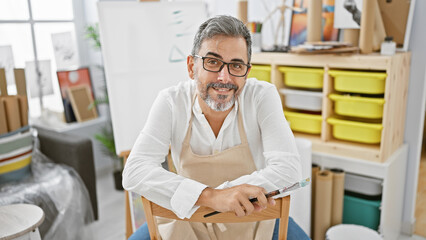 Grey-haired young hispanic man joyfully painting, a bearded artist with glasses, smiling...