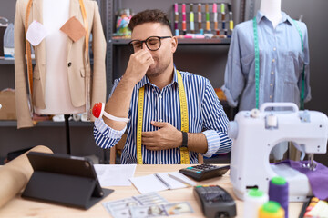 Hispanic man with beard dressmaker designer working at atelier smelling something stinky and...