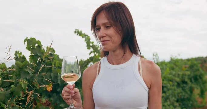 Female winemaker going through vineyard winery with white wine in wineglass, wine tasting and winemaking concept