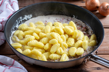 Potato gnocchi in a pan with bacon and sauce on a wooden table.