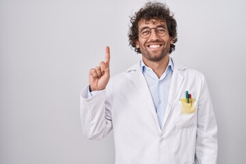 Hispanic young man wearing doctor uniform showing and pointing up with finger number one while smiling confident and happy.
