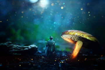 Fototapeta na wymiar Photo of glowing mushrooms at night and small figure walking, mysterious forest, fantasy concept